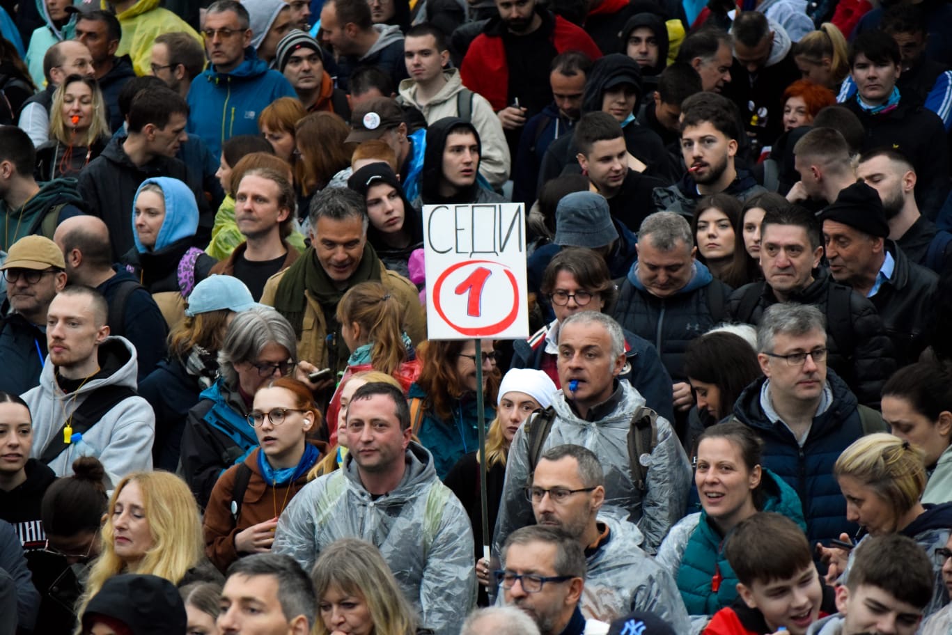 protesters in a crowd, one with a sign saying 'step down'