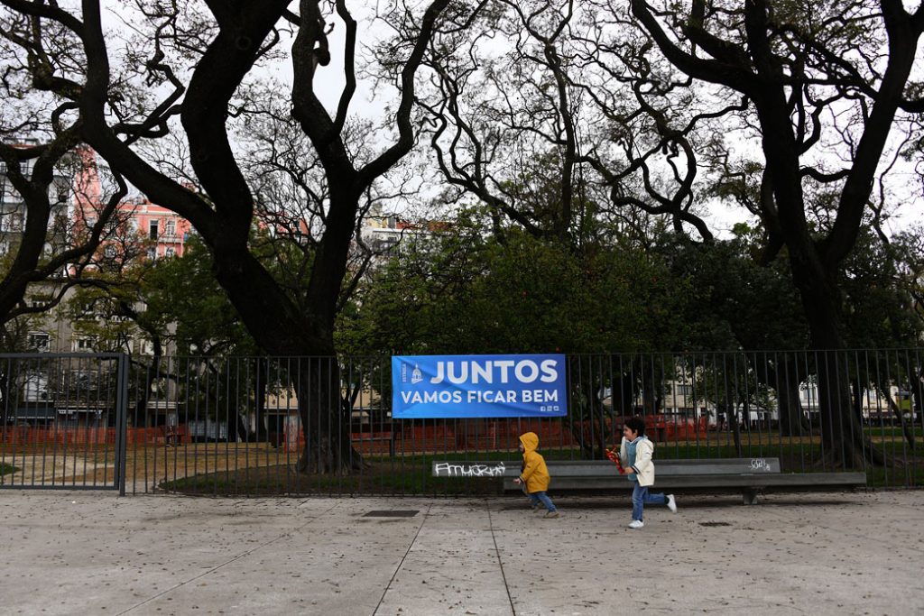 Two children run past a banner that says, "Together, we'll be fine," in Lisbon, April 2020