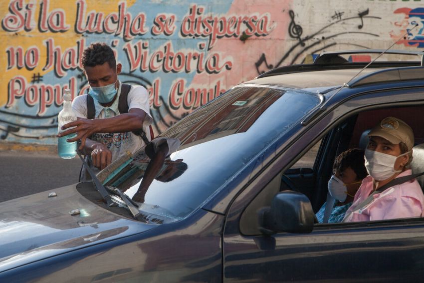 man with a mask washes a car window in Venezuela
