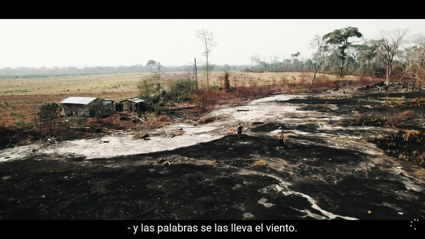 Still from documentary showing scorched earth and a damaged home