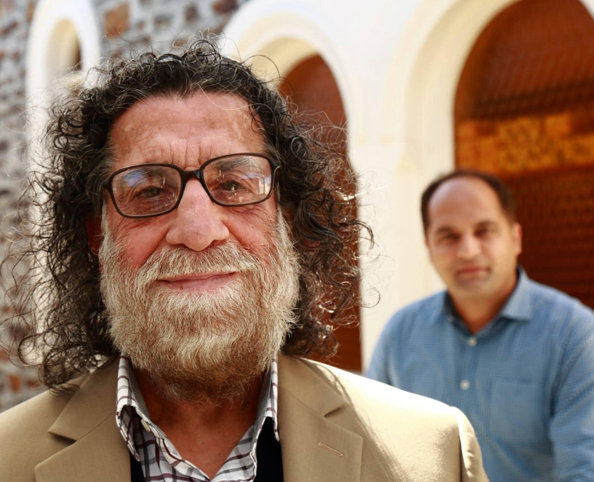 Man with a beard in the foreground. Another man in the background.