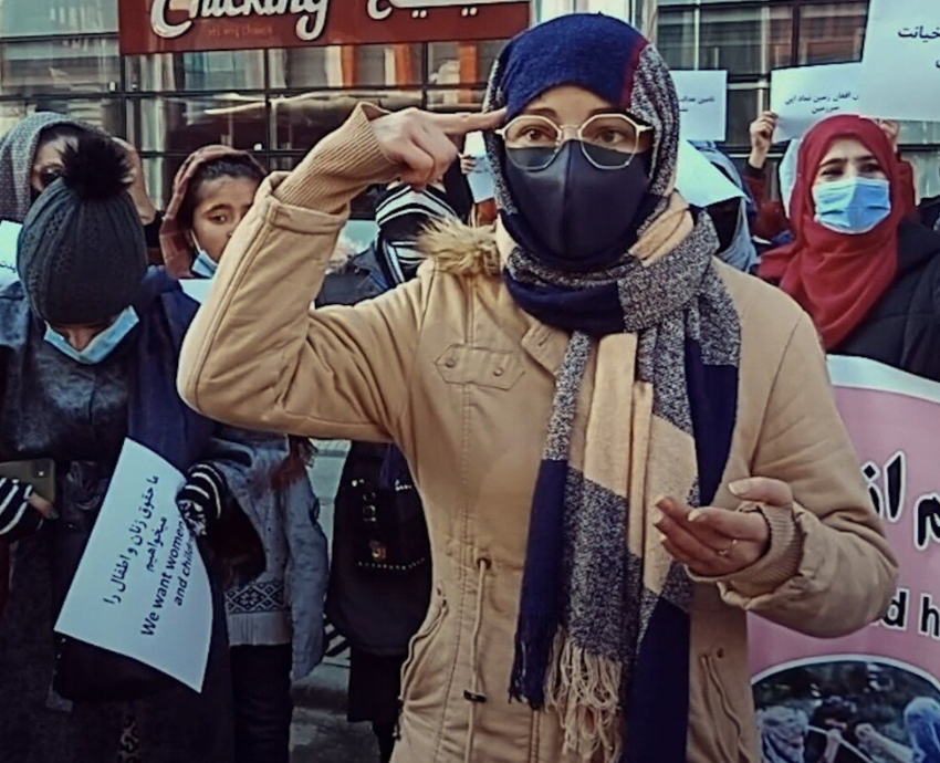 An Afghan woman in a headscarf points her fingers at her head