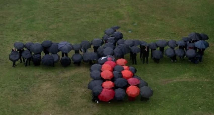 Photo of a black cockatoo formed by people holding black and red umbrellas