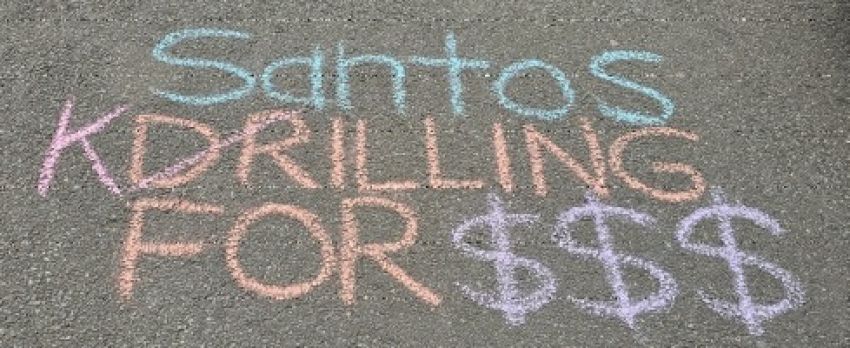 Chalk on footpath that says "Santos Killing for $$$". The letter D for the word Drilling has been crossed out and replaced with K to spell Killing.