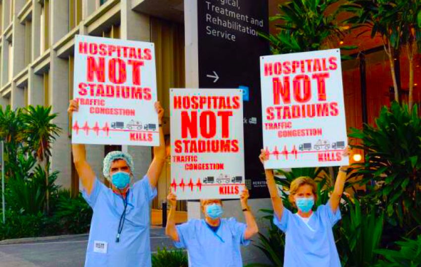 Protesters with signs that say Hospitals Not Stadiums