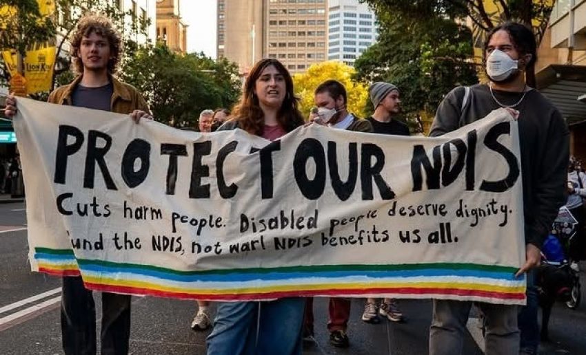 Protesters at a Protect Out NDIS protest holding a banner that say Protect Out NDIS