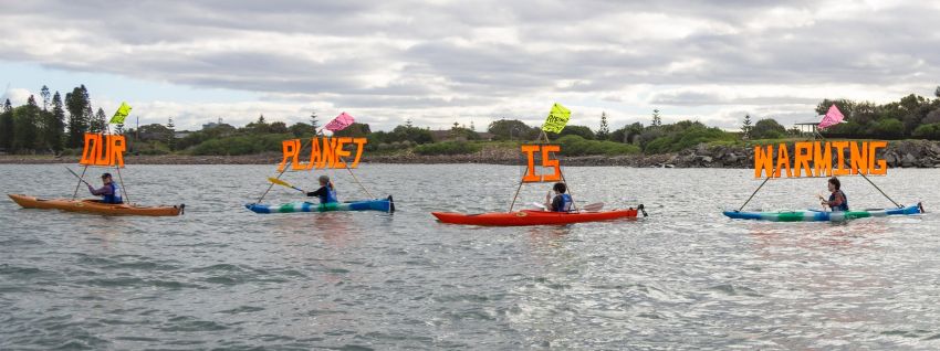 Rising Tide activists on kayaks holding signs that say Our Planet Is Warming