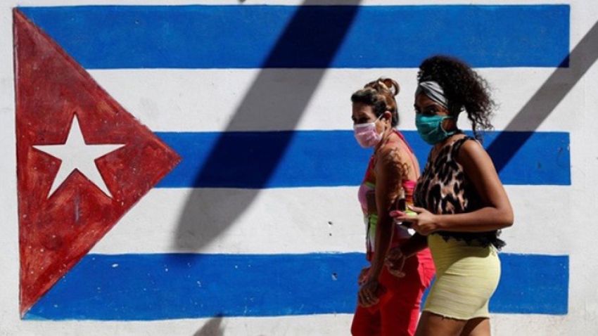 Women walk past a Cuban flag mural.