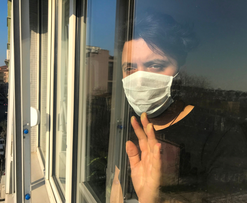 woman wearing a face mask looking out a window