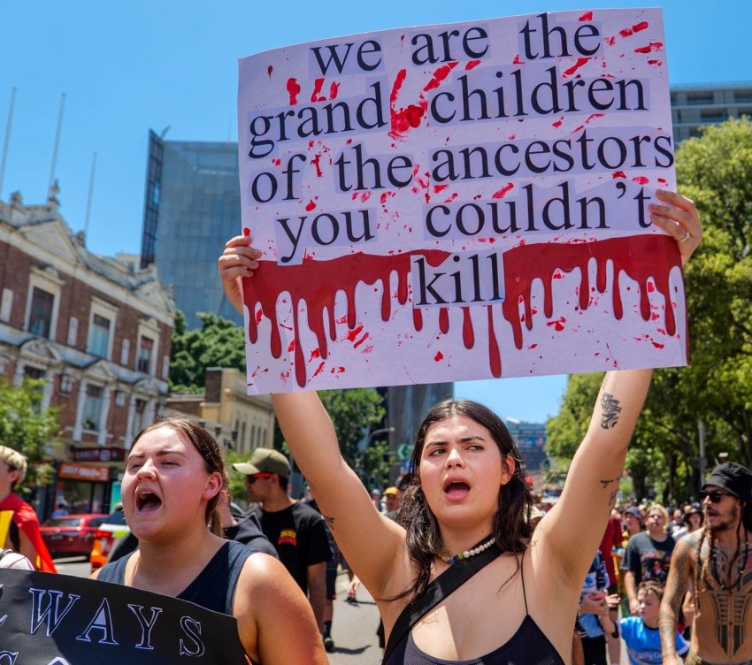 Protester holds sign reading 'We are the grand children of the ancestors you couldn't kill'