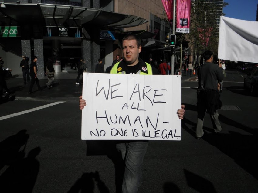 Protester holding sign that says 'We are all human - no one is illegal' at a refugee rights protest.