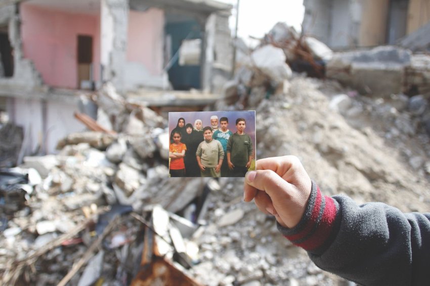 The hand of Yassir Mahmoud El Haj holding a picture of his family in front of the home in which Isra
