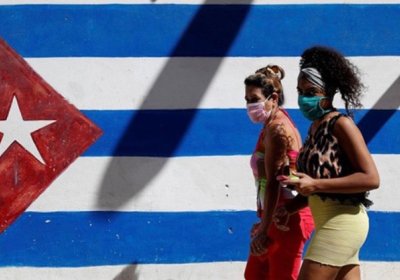 Women walk past a Cuban flag mural.
