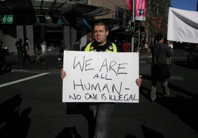Protester holding sign that says 'We are all human - no one is illegal' at a refugee rights protest.