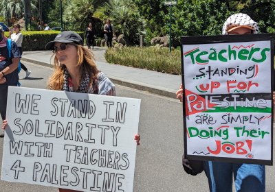 A person holding a sign that says: "We stand in solidarity with Teachers 4 Palestine"