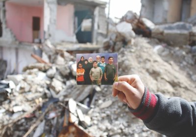 The hand of Yassir Mahmoud El Haj holding a picture of his family in front of the home in which Isra
