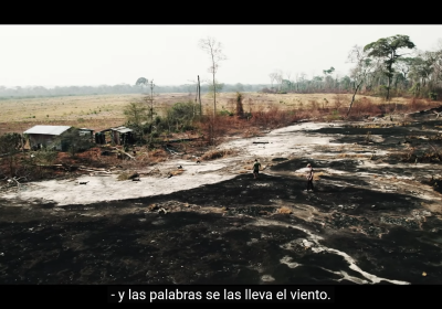 Still from documentary showing scorched earth and a damaged home