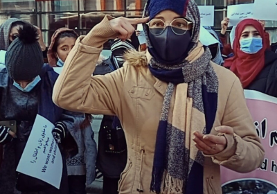 An Afghan woman in a headscarf points her fingers at her head