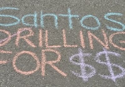 Chalk on footpath that says "Santos Killing for $$$". The letter D for the word Drilling has been crossed out and replaced with K to spell Killing.