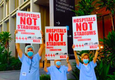 Protesters with signs that say Hospitals Not Stadiums