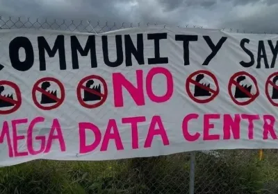 Photo of banner on a fence that reads Community Says NO to Mega Data Centres