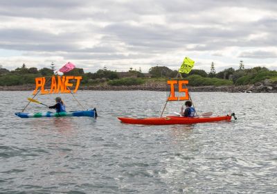 Rising Tide activists on kayaks holding signs that say Our Planet Is Warming